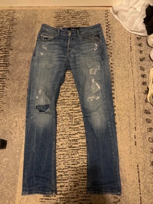 Blå slitna jeans från Replay - Säljer ett par blå jeans från Only & Sons med slitningar och hål på både lår och knän. Jeansen har fem fickor, normal midja och smal passform. Perfekta för en avslappnad och trendig look. Pris kan diskuteras 