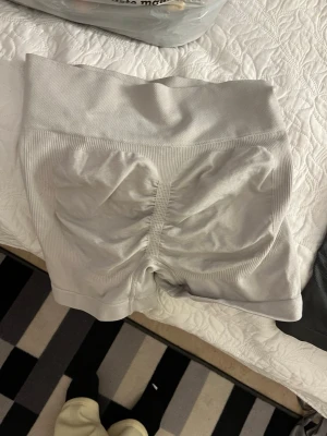 Ljusgrå seamless shorts med scrunch - Säljer ett par ljusgrå seamless shorts med hög midja och scrunch-detalj bak. Shortsen har ribbade partier och ett mönstrat meshparti på baksidan för extra ventilation. Perfekta för träning eller chill. Materialet är stretchigt och följsamt.