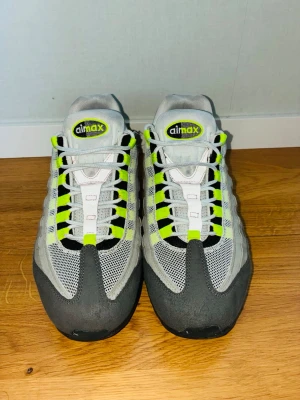Nike Air Max 95 Neon - Nike Air Max 95 Neon med ikoniska detaljer i grått, svart och neongult. Ovandelen är i mesh och mocka med vita och neongula snören. Synlig Air-sula och klassisk logga på plösen. Perfekta sneakers för dig som gillar retrostil och streetwear.