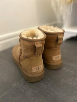 Bruna UGG tofflor i mocka - Mysiga bruna tofflor från UGG i klassisk modell med mjukt fårskinnsfoder och ovandel i mocka. Perfekta för kalla dagar och har en robust sula som ger bra grepp. UGG-logga bak på hälen och enkel slip-on design. Helt oanvända då jag köpte dem i fel storlek🤎