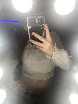 Vit croppad blus med volangärm - Söt vit croppad blus med transparenta, prickiga ärmar och volangdetaljer vid ärmslut och midja. Toppen har smockad rygg och liten öppning bak i nacken. Perfekt för dig som gillar romantisk och trendig stil.