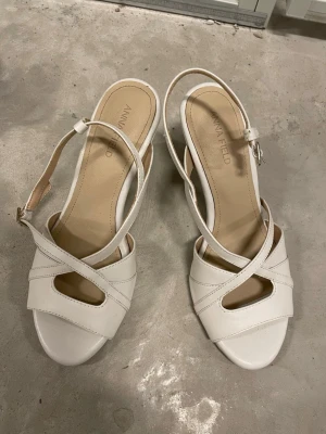Vita sandaler med klack från Anna Field - Snygga vita sandaler från Anna Field med öppen tå och korsade remmar framtill. Sandalerna har en justerbar rem runt hälen och en bekväm, låg klack. Tillverkade i ett slätt material som ger en stilren look.