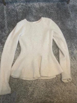 Vit stickad peplumtröja med pärlor - Supersöt vit stickad tröja med peplumskärning och dekorativa pärlor över hela plagget. Tröjan har rund halsringning, långa ärmar och ribbad struktur. Perfekt för dig som vill ha en feminin och trendig look. Pris kan diskuteras och kom privat för mer info eller bilder!💌