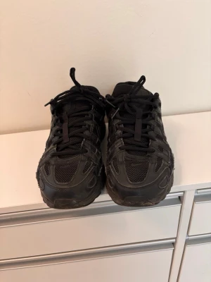 Svarta Nike p6000 - Säljer ett par helsvarta Nike sneakers med cool mesh och läderdetaljer. Skorna har en chunky sula och klassisk Nike Swoosh på sidan. Lågt skaft och snörning framtill. Perfekta för dig som gillar sportig och stilren look.