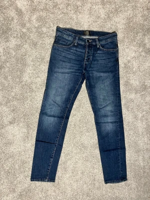 Mörkblå slim fit jeans från Nuew Stocholm - Snygga mörkblå slim fit jeans från Nuew med klassisk femficksdesign och normalhög midja. Jeansen har en lätt tvättad look och slimade ben. Perfekta för dig som gillar en enkel och stilren stil.