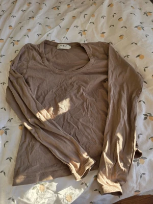 Beige långärmad topp från ICHI - M - En enkel och stilren beige långärmad topp från ICHI. Modellen har rund halsringning och är tillverkad i mjuk bomull som känns skön mot huden. Perfekt att matcha med jeans eller kjol för en clean look.
