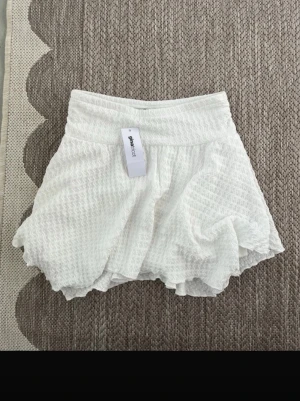 Vit volangkjol från Gina Tricot - Supersöt vit kortkjol från Gina Tricot med volangkant och strukturmönster. Aldrig använd 