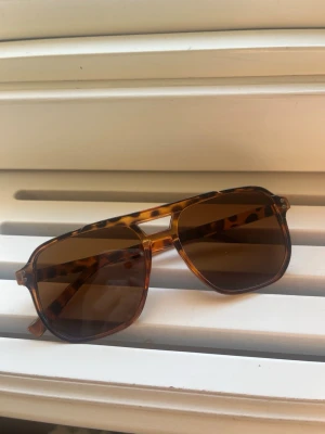 Bruna pilotbågar med leopardmönster - Snygga solglasögon med klassisk pilotform och leopardmönstrad båge i bruna toner. Glasen är mörkbruna och ger en cool retrovibe. Perfekta för soliga dagar när du vill sticka ut lite extra. Säljer eftersom jag av misstag råkade beställa två par.