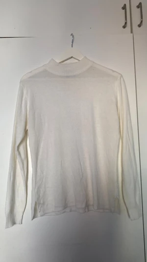Vit stickad tröja - Klassisk vit stickad tröja med lång ärm och ribbade muddar. Tröjan har en högre halsringning och små slitsar i sidorna nedtill för en snygg detalj. Perfekt att matcha med jeans eller kjol för en clean look. Står XL på lappen men skulle säga att den passar M och uppåt 