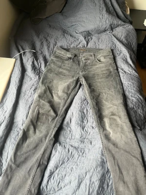 Grå slim fit jeans från Nudie - Snygga grå slim fit jeans från Nudie Jeans med klassisk femficksmodell och diskreta sömmar. Jeansen har en något tvättad look och är tillverkade i ett mjukt denimtyg som sitter skönt. Perfekta för dig som gillar stilrena och moderna jeans.