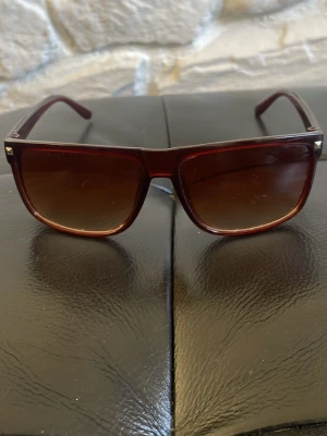 Bruna fyrkantiga solglasögon - Snygga solglasögon med fyrkantig form och bruna bågar. Glasen är tonade i brunt och bågarna har en diskret glansig finish. Perfekta för dig som vill ha en stilren accessoar med en klassisk vibe. 