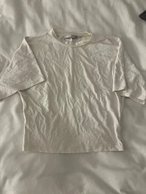 Vit basic t-shirt från 157 - En enkel vit t-shirt från 157 med rund hals och korta ärmar. Tillverkad i mjukt bomullsmaterial som känns skönt mot huden. Perfekt att matcha med jeans eller shorts för en clean och avslappnad stil.