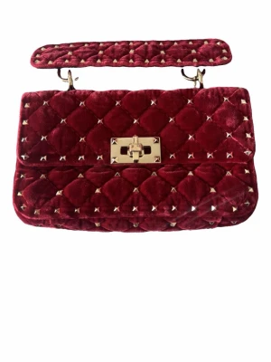 Röd sammetsväska med nitar - Säljer denna jätte snygga valentino väska, köpt på vestaire för några månader sen för 8500. Har dessvärre tappat bort dustbagen som kom med. Snygg handväska i mörkröd sammet med quiltat mönster och små guldfärgade nitar. 