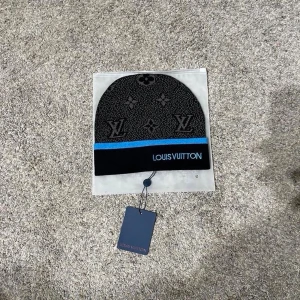 Svart mössa - Snygg svart mössa med klassiskt mönster och logga framtill. Mössan har en blå rand och är tillverkad i mjukt material som känns lyxigt. Perfekt accessoar för dig som gillar exklusiv streetwear.