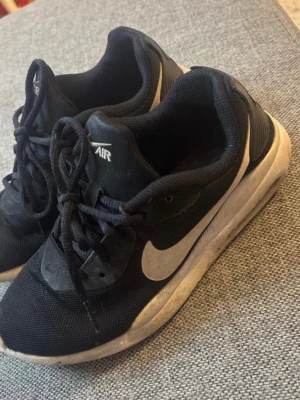 Svarta Nike Air sneakers med vit sula - Säljer ett par svarta Nike Air sneakers med vit sula och klassisk vit swoosh på sidan. Skorna har snörning och är tillverkade i mesh och syntetmaterial för en sportig look. Perfekta för dig som gillar streetwear och bekväma skor.