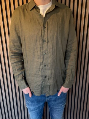 Olivgrön linneskjorta från Massimo Dutti - Säljer en olivgrön skjorta i linne med klassisk krage och knäppning framtill. Skjortan har lång ärm och en avslappnad passform, perfekt för en stilren och enkel look. Skjortan är använd en gång, och är från Massimo Dutti! skicka dm vid frågor!