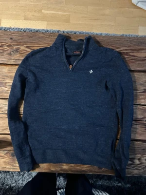 Morris halfzip  - Snygg mörkblå stickad tröja från Morris med halv dragkedja och ribbad krage. Tröjan har en liten broderad logga på bröstet och ribbade muddar vid ärmslut och nederkant. Perfekt för lager på lager och stilren look.
