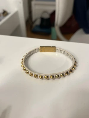 Nit armband Edblad - Guldfärgat och vitt nit armband från Edblad. Använt men i fortfarande mycket fint skick. Det har skavts av lite på insidan, vilket kan ses på bilderna. Annars inga större defekter. Armbandet är ca 20cm långt. Skriv gärna vid frågor eller funderingar💕Asken på bilden medföljer inte. 