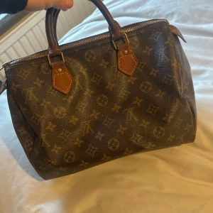 Louis Vuitton Speedy Monogram väska - Klassisk Louis Vuitton Speedy handväska i brunt monogrammönstrat canvas med detaljer i läder. Väskan har två robusta handtag, guldfärgade metalldetaljer och dragkedja upptill. Modellen är Louis Vuitton Monogram Speedy 30 Bag. Pris går att diskuteras