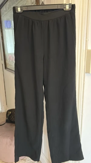 Svarta vida kostymbyxor - Säljer ett par svarta kostymbyxor med resår i midjan och raka, vida ben. 