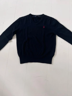 Mörkblå V-ringad tröja Polo Ralph Lauren - Klassisk mörkblå V-ringad tröja från Polo Ralph Lauren med den ikoniska röda loggan broderad på bröstet. 