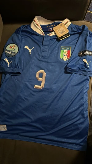 Italien Euro 2012 fotbollströja #9 Balotelli -  Italien fotbollströja från Euro 2012 med nummer 9 och Balotelli på ryggen. Tröjan har vita detaljer, broderad landslagssköld, Puma-loggor och patchar på. perfekt för match eller träning. Storlek M och har enbart använts vid få tillfällen 