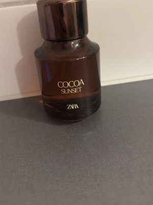 Cocoa Sunset parfym från Zara - Cocoa Sunset från Zara är en parfym i en brun glasflaska med metalliskt lock. Flaskan har en rundad form och stilren design. Doften ger en lyxig känsla och flaskan är perfekt att ha framme på sminkbordet.