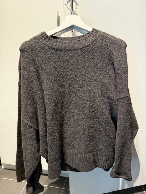 Mörkgrå stickad tröja Vero Moda - Mysig mörkgrå stickad tröja från Vero Moda med avslappnad passform och bred ribbad mudd vid hals, ärmslut och nederkant. Tillverkad i mjukt material som känns skönt mot huden. Perfekt för kyliga dagar.