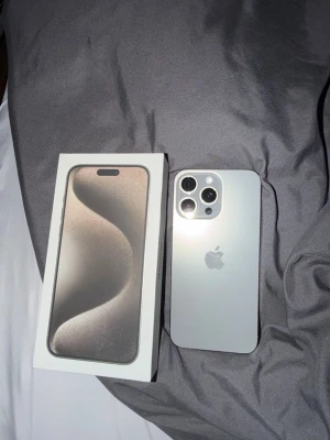 Silver iPhone med platt design  - Säljer en stilren silverfärgad iPhone med platt design och tre stora kameror på baksidan. Telefonen har en elegant glasbaksida och metallram, perfekt för dig som gillar modern teknik och snygg design.