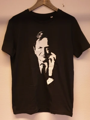 Svart t-shirt med Olof Palme tryck - Cool svart t-shirt från Stanley/Stella med ett stort vitt Palme tryck på framsidan. Gjord i mjuk ekologisk bomull och har klassisk rund hals och korta ärmar. Perfekt för dig som gillar stilrena och grafiska motiv.