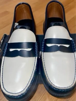 Marinblå och vita loafers från Marni - Säljerww ett par stilrena loafers från Marni i marinblått och vitt läder. Skorna har klassisk pennyloafers-design med kontrasterande mörkblå rem över vristen och vita ovandelar. Snygga detaljer med blå sömmar och robust sula. Perfekta för dig som gillar en clean och modern look. Köpte 3000kr