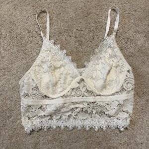 Vit spetsbralette från SHEIN - Säljer en vit spetsbralette från SHEIN med tunna axelband och vackra blommiga spetsdetaljer. Braletten har dekorativ kant nertill och är tillverkad i ett genom sopigt spetsmaterial som ger en romantisk look.