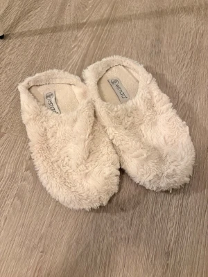 Krämvita fluffiga tofflor Esmara - Mysiga krämvita tofflor från Esmara i supermjuk fuskpäls. De har en enkel slip-in design och är perfekta för att hålla fötterna varma hemma. Tofflorna har en låg profil och är helfodrade för extra komfort.