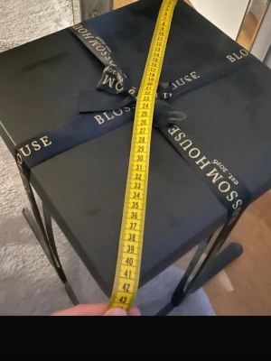 Nalle av rosor i presentbox Blossomhous - Säljer en grå nallebjörn gjord av konstgjorda rosor med ett rött hjärta på magen. Nallen kommer i en svart fyrkantig presentbox med genomskinliga sidor och svart band med guldtext. Perfekt som unik present eller dekoration.