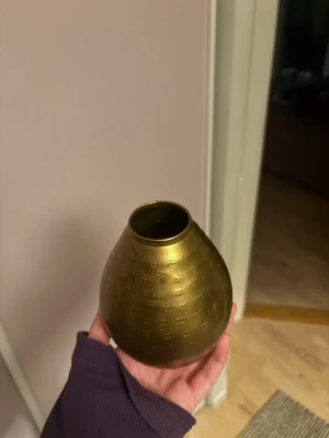 Liten rund mässingsvas 💐 - Säljer en liten rund vas i mässing med diskret mönster runt om. Vasen har en gyllene färg och en smal öppning upptill, perfekt som dekoration eller för enstaka blommor.