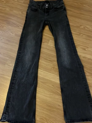 Svarta bootcut jeans med slitningar - Säljer ett par svarta bootcut jeans med lätt slitna detaljer och klassisk femficksmodell. Jeansen har vida ben och knappgylf. Perfekta för dig som gillar en avslappnad och trendig look.