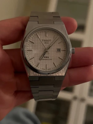 Tissot herrklocka i rostfritt stål - Snygg Tissot herrklocka med länkarmband i rostfritt stål. Klockan har en klassisk, stilren design med silverfärgad finish och robust metallarmband. Perfekt accessoar för dig som gillar tidlös och elegant stil. Extra länkar ingår. Ingen box. 