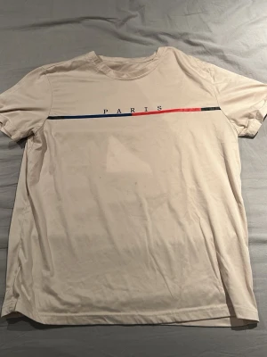 Beige t-shirt med PARIS-tryck - Lite fläckig på magen.