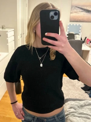 Svart stickad croppad topp - En enkel och stilren svart stickad tröja med korta ärmar och rund hals. Tröjan har en något croppad passform och är perfekt att matcha med jeans eller kjol. Materialet är mjukt och bekvämt , idealiskt både en avslappnad look och en uppklädd look.