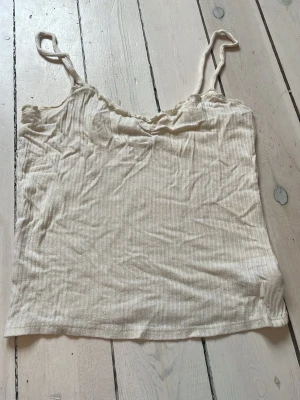 Beige ribbad linnetopp - Säljer en enkel och stilren beige linnetopp med smala axelband och ribbad struktur. Perfekt att matcha med jeans eller kjol för en avslappnad look. Materialet känns mjukt och följsamt mot huden.