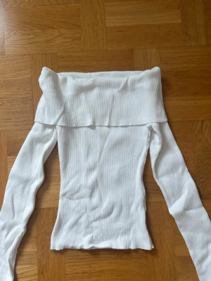 Vit ribbad offshoulder topp - Trendig vit ribbad topp med offshoulder-design och långa ärmar. Perfekt för dig som gillar en stilren och enkel look. Materialet är stretchigt och sitter snyggt på kroppen.