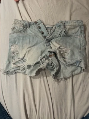 Ljusblåa slitna jeansshorts med knappar -  Säljer ett par ljusblå shorts från H&M, men det står inte storlek. Skulle gissa på ca XS eller XXS