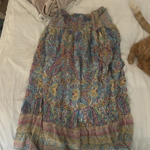 Mönstrad lång kjol - Färgglad långkjol med ett livfullt mönster i blått, gult och rosa. Kjolen har en elastisk midja för bekväm passform och är perfekt för en bohemisk stil.