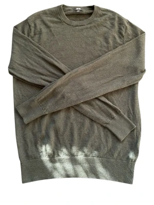 Olivgrön stickad tröja Uniqlo - Olivgrön stickad tröja från Uniqlo med rund hals och ribbade muddar vid ärmslut och nederkant. Tröjan är tunn och har en enkel, clean look som passar perfekt till lager-på-lager. Materialet känns mjukt och smidigt.