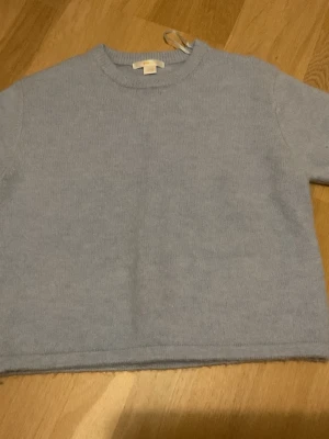 Ljusblå stickad tröja - En enkel och stilren ljusblå stickad tröja med rund halsringning och raka ärmar. Tröjan har en croppad passform och är tillverkad i ett mjukt stickat material. Perfekt för lager-på-lager och passar till många olika outfits.