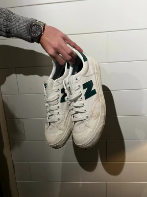 New Balance sneakers - Snygga vita New Balance sneakers med gröna detaljer och klassisk N-logga på sidan. Skorna har lågt skaft, vita snören och en robust sula. Perfekta för dig som gillar en clean och sportig stil. Ovandelen är i textil och mocka.