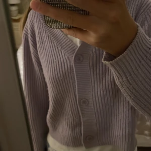 Ljuslila stickad kofta från KappAhl - Supersöt ljuslila stickad kofta från KappAhl med ribbad struktur och v-ringning. Koftan är croppad, har långa ärmar och stängs med tre knappar framtill. Perfekt att slänga över en t-shirt för en chill look. Står stl 158/164, men passar mig som har XS-S. Köpt på Kappahl och har inte använt jättemycket men den är lite nopprig, men det förstör inte helheten. Hör av er om frågor!❤️