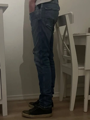 Blå slim fit jeans med kontrastsömmar - Säljer ett par blå slim fit jeans med tydliga kontrastsömmar och klassiska fem fickor. Jeansen har en något tvättad look och sitter tight längs benen för en modern siluett. Perfekta för dig som gillar en enkel men snygg stil.
