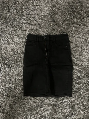 Svart jeanskjol med fickor - Snygg svart jeanskjol från Ginatricot med klassisk femficksmodell, bälteshällor och dragkedja framtill. Kjolen är kort och har en rak passform som passar till många olika stilar. Perfekt basplagg i garderoben.