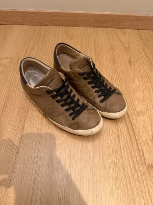 Phillipe model - Säljer ett par bruna sneakers från Saint Laurent i läder med svarta snören och vit sula. Skorna har en klassisk låg profil och diskreta detaljer på sidan. Perfekta för dig som gillar stilrena och tidlösa sneakers.